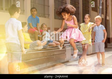 Energetic kids playing and skipping on elastic jumping rope in yard Stock Photo