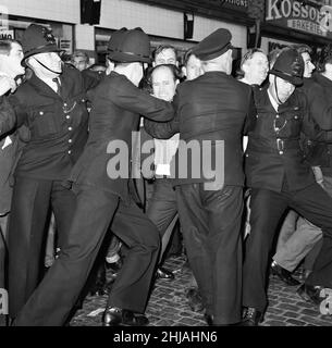 A large crowd gathered in Ridley Road, E8 to demonstrate against former fascist leader Sir Oswald Mosley and members of his anti-Semitic Blackshirt group who had planned a rally in London's East End. Mosley and his group were assaulted and punched to the ground as soon as his meeting opened at Ridley Road, Dalston. Police closed the meeting within the first three minutes and made 54 arrests, one of which was Sir Oswald's son Max.  Police hold back one of the angry demonstrators. 31st July 1962. Stock Photo