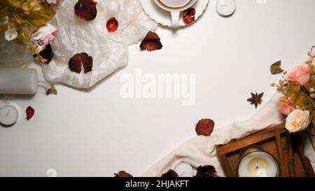 Red roses compositions with decorations on white background. Feminine workspace with roses, tea cup, candles, textile and copy space on white backgrou Stock Photo