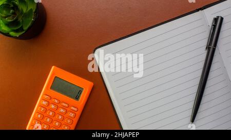 Flat layout of blank paper sheet, notebooks, calculator and pen on brown leather background. Home office desk workspace. Business, work template. Flat Stock Photo