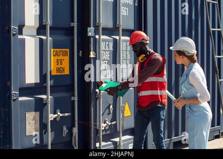 Businesswoman and engineer talking and checking loading Containers box from Cargo freight ship for import export. shipping in docks. Stock Photo