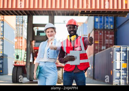 Businesswoman and engnineer showing thumbs up with laptop working at warehouse container cargo ship import export industry. Stock Photo