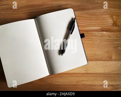 A grid journal with a ballpoint pen on a wood table Stock Photo