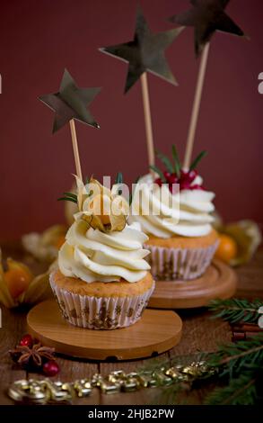 Christmas cupcakes with vanilla frosting, cranberries and rosemary on wooden background Stock Photo