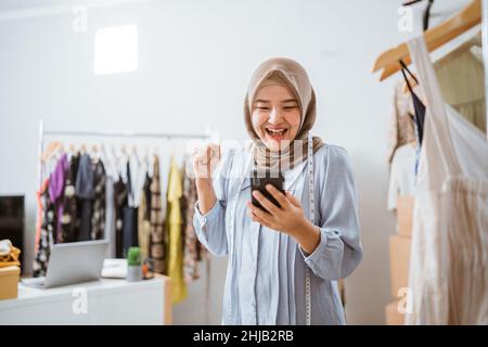excited asian muslim woman small business owner look at phone Stock Photo