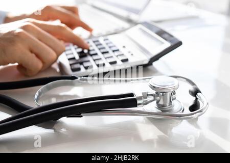 Businessman Calculating Invoice With Stethoscope On Documents At Table Stock Photo