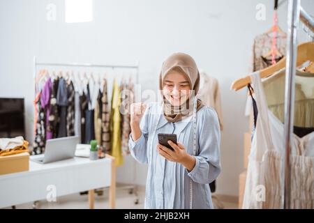 excited asian muslim woman small business owner look at phone Stock Photo
