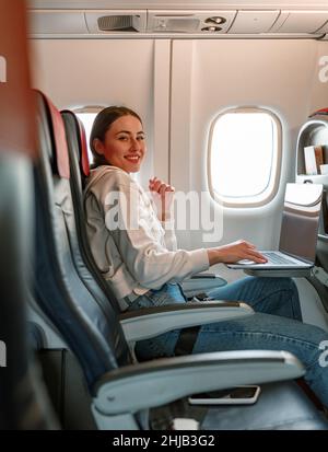 Joyful young woman using notebook in airplane Stock Photo