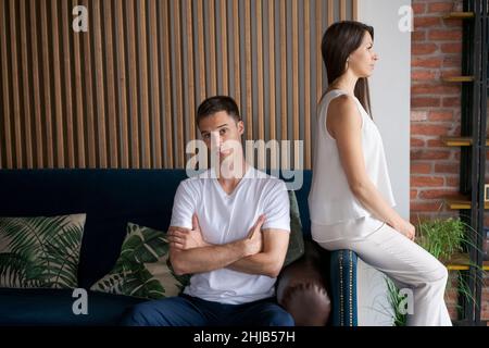 Sad middle aged couple after quarrel at home. Caucasian family sitting on couch turned away from each other from resentment. Conflict concept in a young family Stock Photo