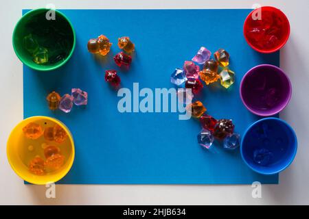 Multicolored toy stones scattered on blue surface and colorful cups for separating by color Stock Photo