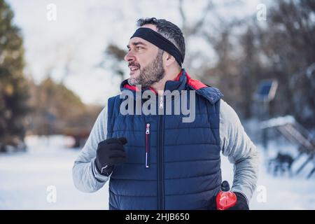 Adult man is exercising in park in wintertime. He is jogging. Stock Photo