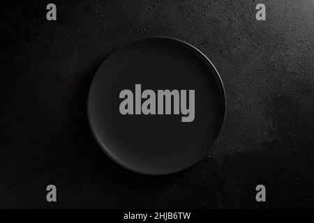 Empty black plate on black textured background. Moody, top down view. Stock Photo