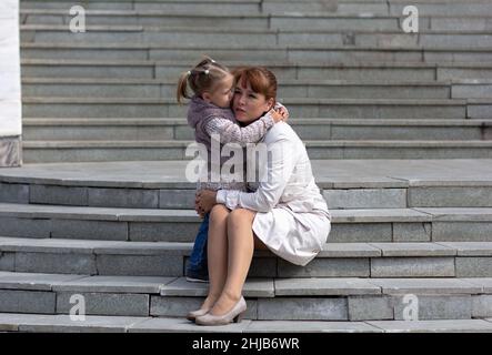 Child hugging mother and looking at her with love on stairs Stock Photo