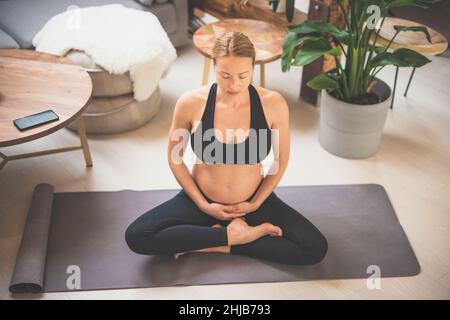 Young beautiful pregnant woman training yoga, caressing her belly. Young happy expectant relaxing, thinking about her baby and enjoying her future Stock Photo