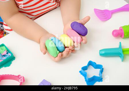 close up children's hands with colored plasticine, play dough, molds for modeling on white background, home creative educational games concept Stock Photo