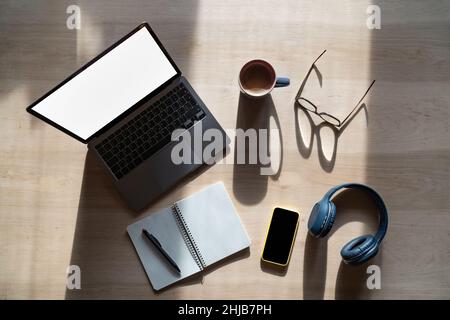 Freelancer workplace mockup on wooden table with laptop, tablet, headphones, glasses, coffee, top view Stock Photo