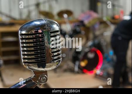 Retro style chrome microphone with drum kit defocused in background Stock Photo