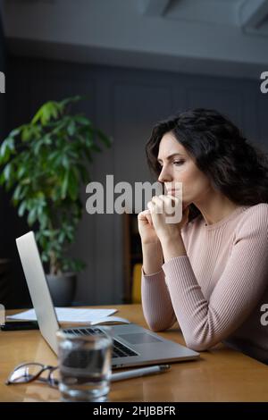 Young focused businesswoman looking at laptop screen, upset female employee thinking about solution Stock Photo