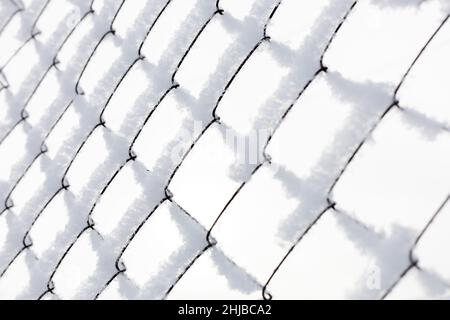 Steel mesh fence slightly covered with snow on white background surrounding restricted area where access for ordinary people is denied. Exile to Stock Photo