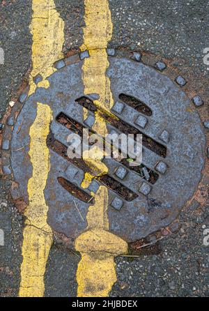 Drainage cover, manhole cover, yellow lines, cast iron cover, blocked drain, road drain, requires maintenance, sewers, combined system, curtilage. Stock Photo