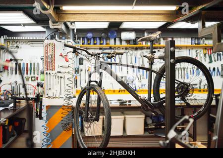 Broken bike placed on rack against workbench with tools in professional bicycle repair shop. Stock Photo