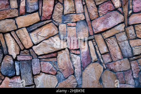The wall is made of multi-colored natural stone, the masonry is stone on cement. Concept - stone wallpaper, background and decor Stock Photo