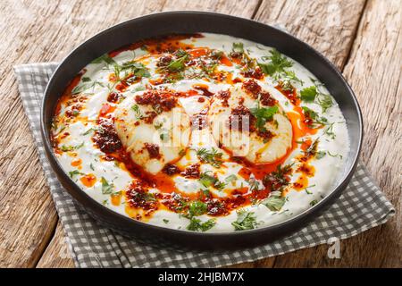Cilbir is a Turkish eggs containing garlicky yogurt, poached eggs, and spiced melted butter in the plate on the wooden table. Horizontal Stock Photo