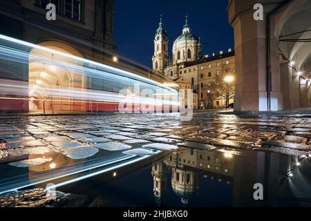 Light trail of tram passing between historic buildings. Reflection in puddle on wet road. Lesser Town in Prague, Czech Republic. Stock Photo