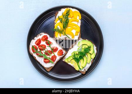 Variety of sandwiches for breakfast - slice of whole grain dark bread, yellow bell pepper, cream cheese, avocado, cherry tomatoes, garnished with dill Stock Photo