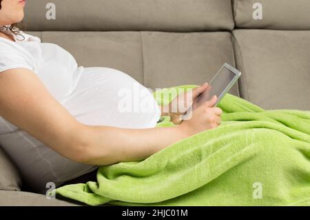 Closeup shot of a pregnant woman texting on her tabet at home Stock Photo