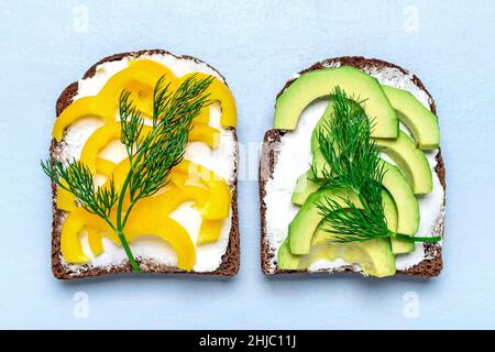 Variety of sandwiches for breakfast - slice of whole grain dark bread, yellow bell pepper, cream cheese, avocado garnished with green dill on blue Stock Photo