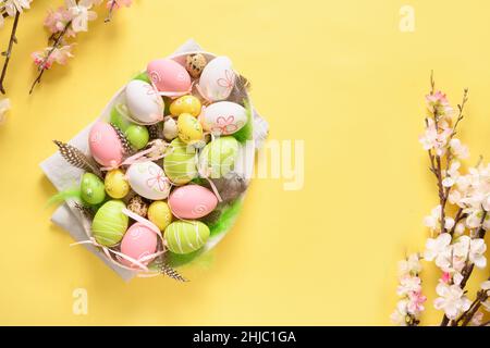 Easter pastel coloful eggs and spring blooming flowers on yellow background with copy space. View from above. Easter greeting card. Stock Photo