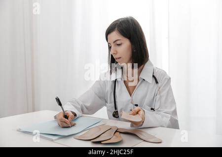 Doctor holding an insole while sitting at a table. Orthopedist tests the medical device. Orthopedic insoles. Foot care. Flat Feet Correction Stock Photo