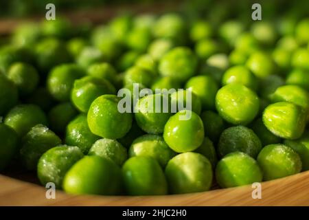 frozen frosty green peas on wooden plate closeup. Stock Photo