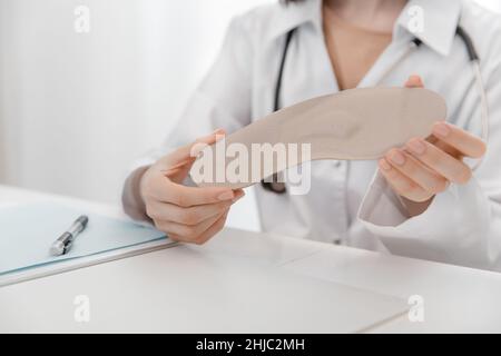 Doctor holding an insole while sitting at a table. Orthopedist tests the medical device. Orthopedic insoles. Foot care. Flat Feet Correction Stock Photo