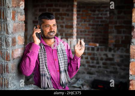 Happy smiling construction labour talking on mobile phone - concept of communication network and technology Stock Photo
