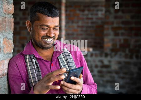 Happy smiling construction worker buys using mobile phone at site showing with copy space - concept of daily wager using smartphone, technology and Stock Photo