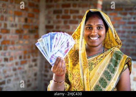 Happy smiling Indian woman with currency notes looking at camera - concept of daily wager or construction woker earnings, banking and financial Stock Photo