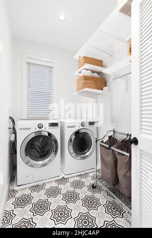 A laundry room with white washer and dryer, a patterned tile floor, and organized shelving on the wall. Stock Photo