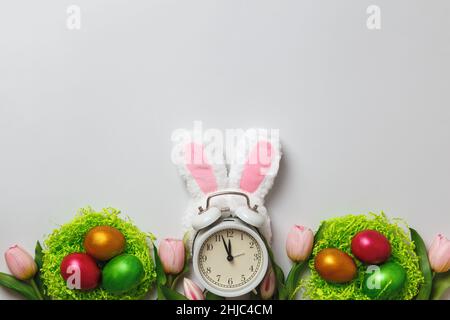 Easter concept. Multi-colored pearl eggs in nests flowers tulips alarm clock on a gray background. Copy space Stock Photo