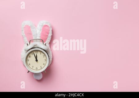 Alarm clock in easter bunny ears on a pink background with copy space. Stock Photo