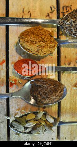 A variety of spoons with different spices on them set against a wooden background. Stock Photo