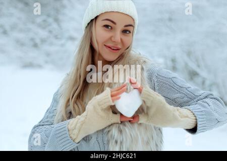 I like winter. Portrait of a happy young girl holding a snowy heart in her hand during winter time. Valentine's Day. Stock Photo