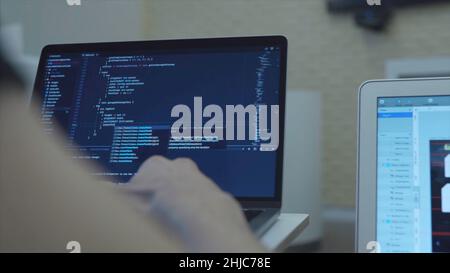 Close-up of web developer's hands programming Javascript, coding HTML on laptop. View from back Stock Photo