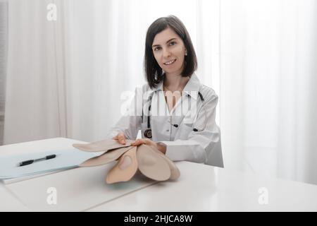 Doctor holding an insole while sitting at a table. Orthopedist tests the medical device. Orthopedic insoles. Foot care. Flat Feet Correction Stock Photo