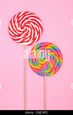 Two colorful round lollipops on sticks, on a soft pink background. The vertical composition. Stock Photo