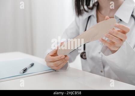 Doctor holding an insole while sitting at a table. Orthopedist tests the medical device. Orthopedic insoles. Foot care. Flat Feet Correction Stock Photo