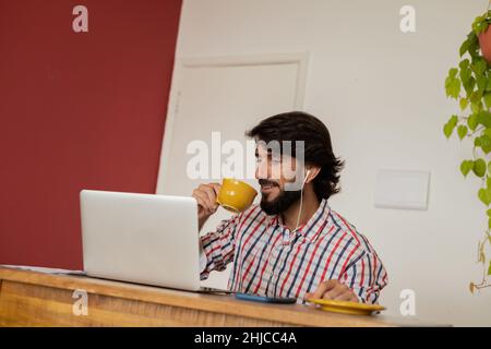 Young business man working at home with laptop and papers on desk while drinking coffee in a yellow cup. Gray notebook for working. Home office concep Stock Photo