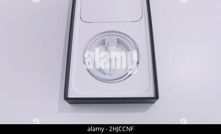Ottawa, Canada - 11.24.2020 opened box of an Apple iPhone on a white table background. Top view of a white charging cable inside the smartphone box. Stock Photo