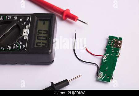 Electronic charging circuit with multimeter with red and black poles, checking voltage and amps, white background. Stock Photo